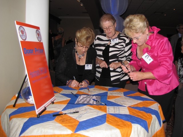 Barbara Tomasini, Janet Daone & Carol Caruba autograph the Door Prize quilt.